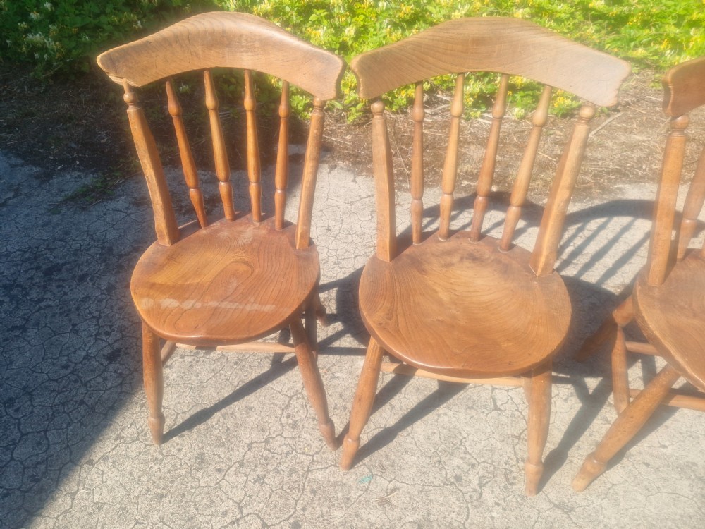 A set of four early twentieth century wooden farmhouse kitchen chairs with spindle backs and carved saddle seats. View III