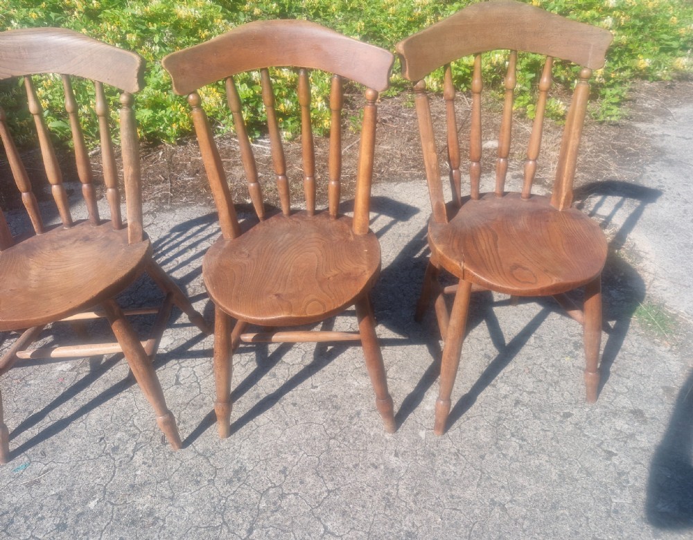 A set of four early twentieth century wooden farmhouse kitchen chairs with spindle backs and carved saddle seats. View IV
