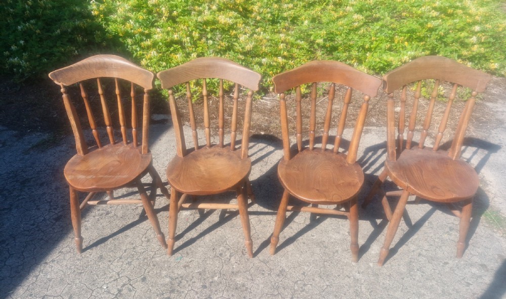 A set of four early twentieth century wooden farmhouse kitchen chairs with spindle backs and carved saddle seats. View V