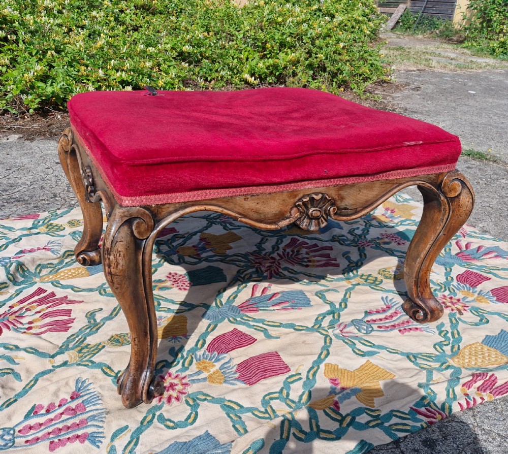 A mid-19th-century carved hardwood centre stool featuring cabriole legs with scroll feet, a decorative floral apron carving, and a crimson red velvet cushion.
