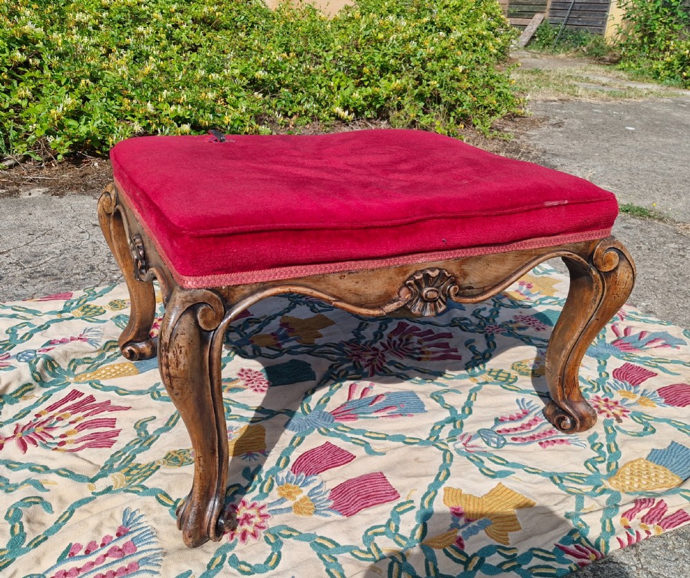 A mid-19th-century carved hardwood centre stool featuring cabriole legs with scroll feet, a decorative floral apron carving, and a crimson red velvet cushion. View II