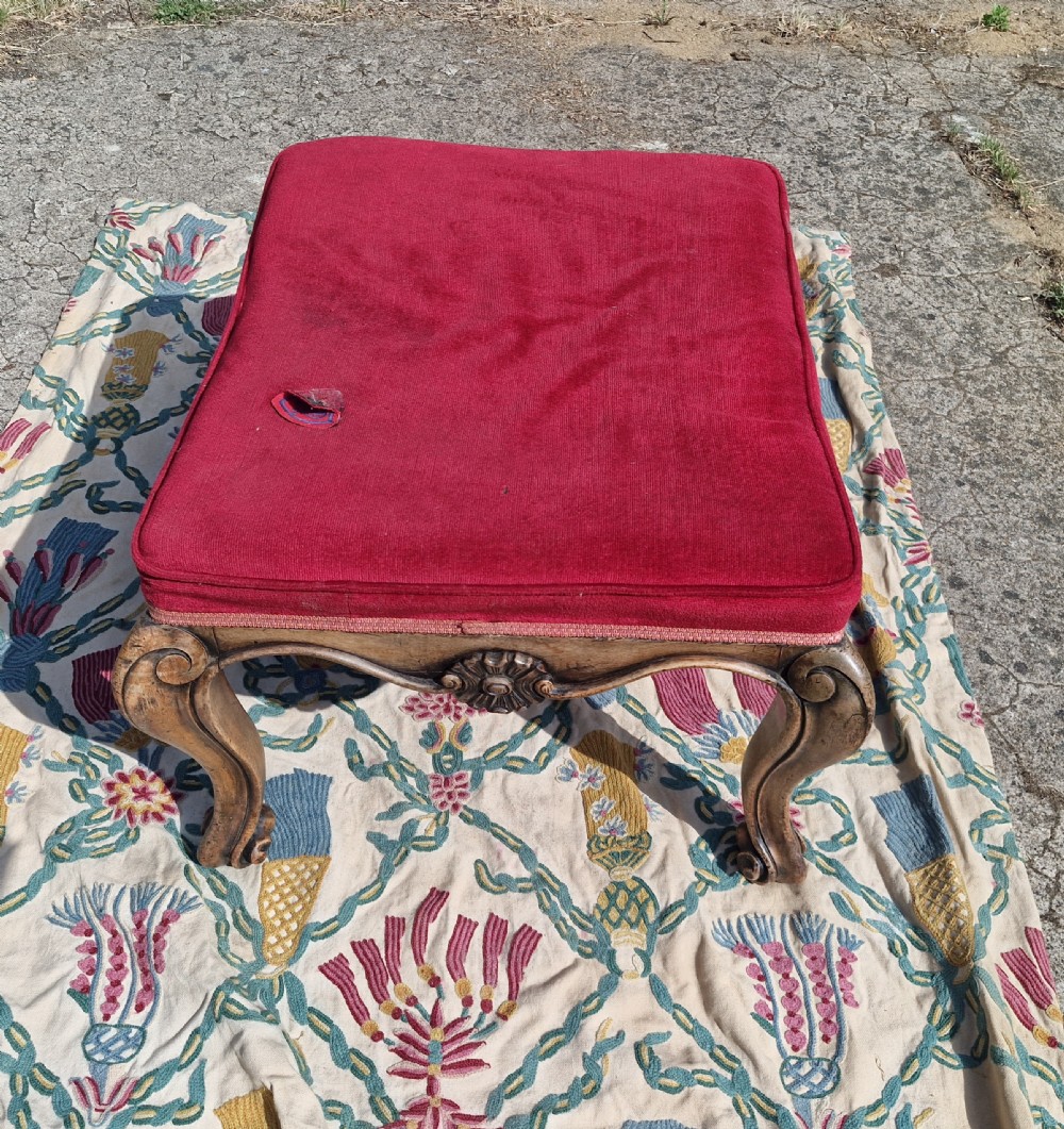 A mid-19th-century carved hardwood centre stool featuring cabriole legs with scroll feet, a decorative floral apron carving, and a crimson red velvet cushion. View III