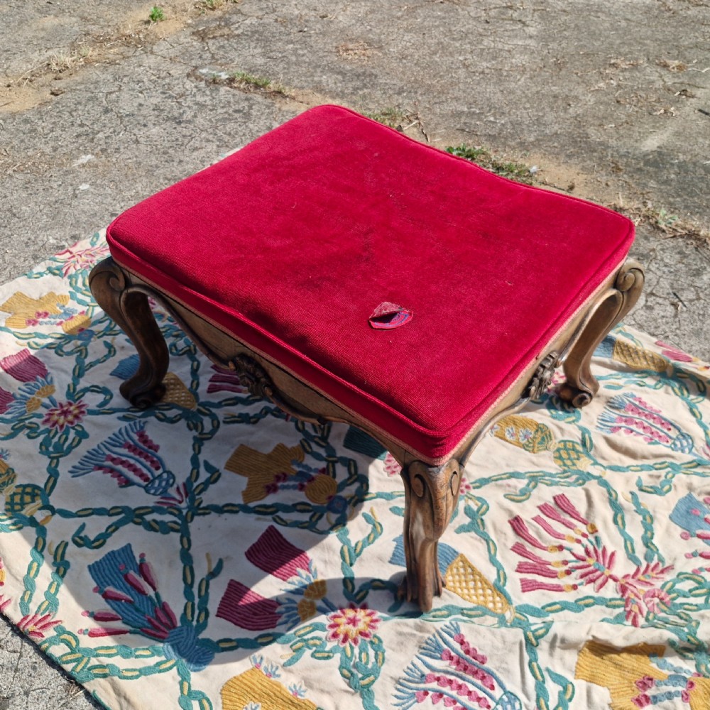 A mid-19th-century carved hardwood centre stool featuring cabriole legs with scroll feet, a decorative floral apron carving, and a crimson red velvet cushion. View IV