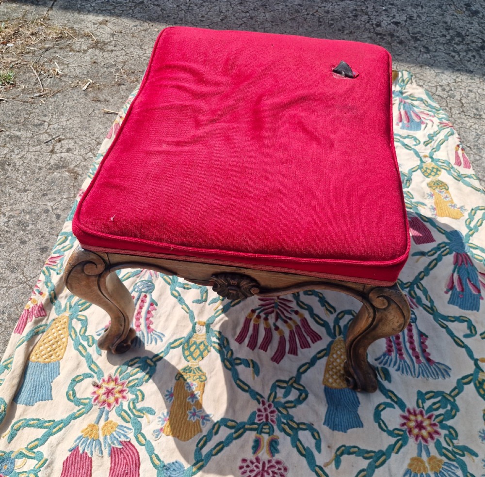 A mid-19th-century carved hardwood centre stool featuring cabriole legs with scroll feet, a decorative floral apron carving, and a crimson red velvet cushion. View V