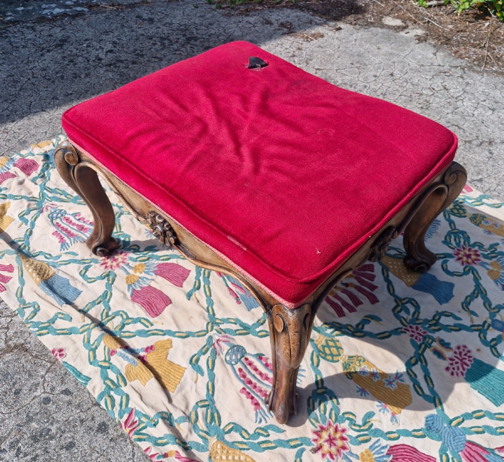 A mid-19th-century carved hardwood centre stool featuring cabriole legs with scroll feet, a decorative floral apron carving, and a crimson red velvet cushion. View VI
