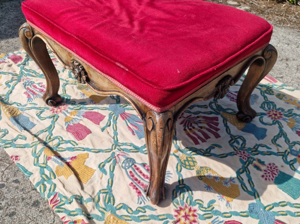 A mid-19th-century carved hardwood centre stool featuring cabriole legs with scroll feet, a decorative floral apron carving, and a crimson red velvet cushion. View VII