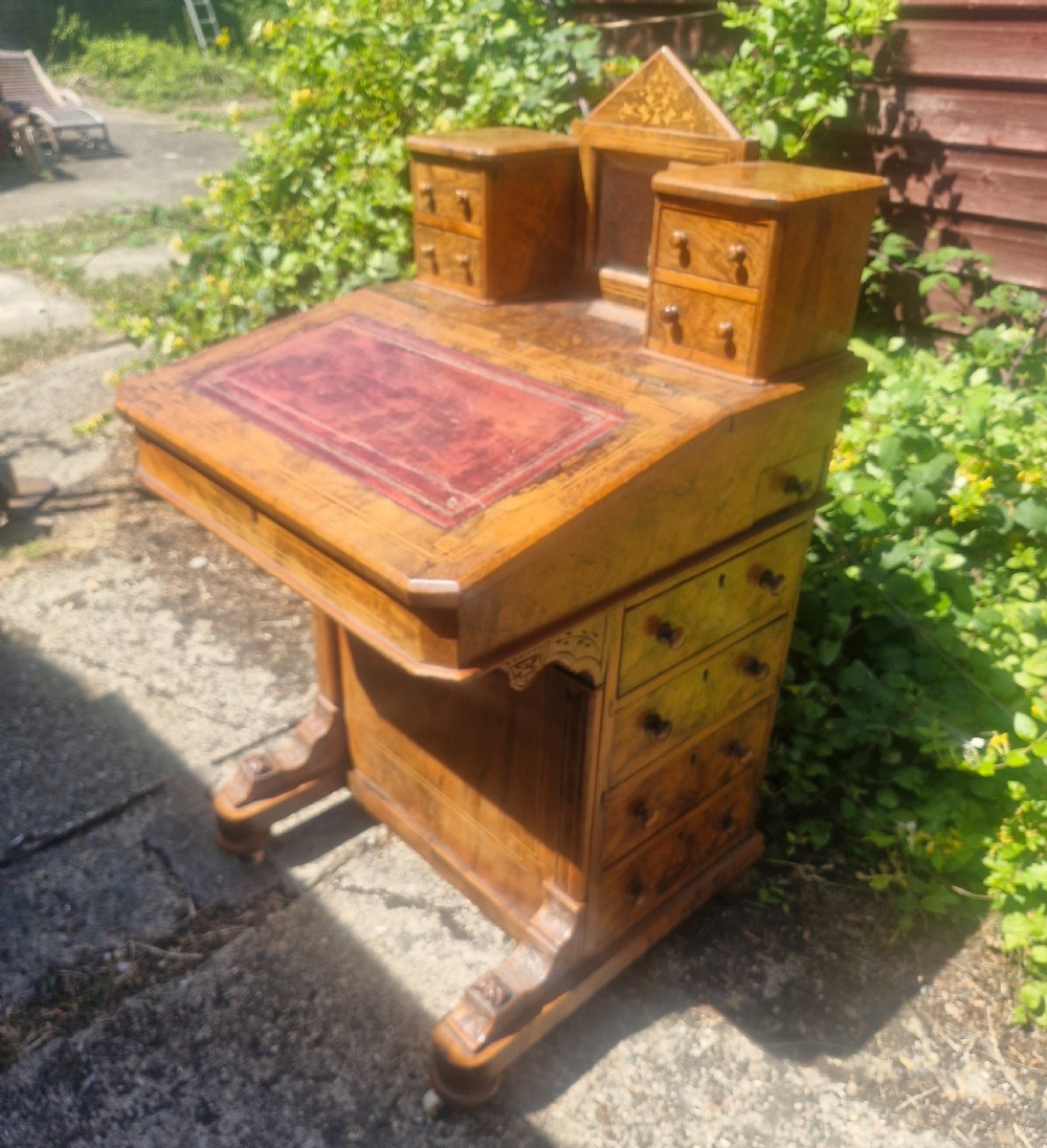 A Victorian burr walnut Davenport desk with a sloped red leather writing surface, inlaid top cresting, and side drawers.
