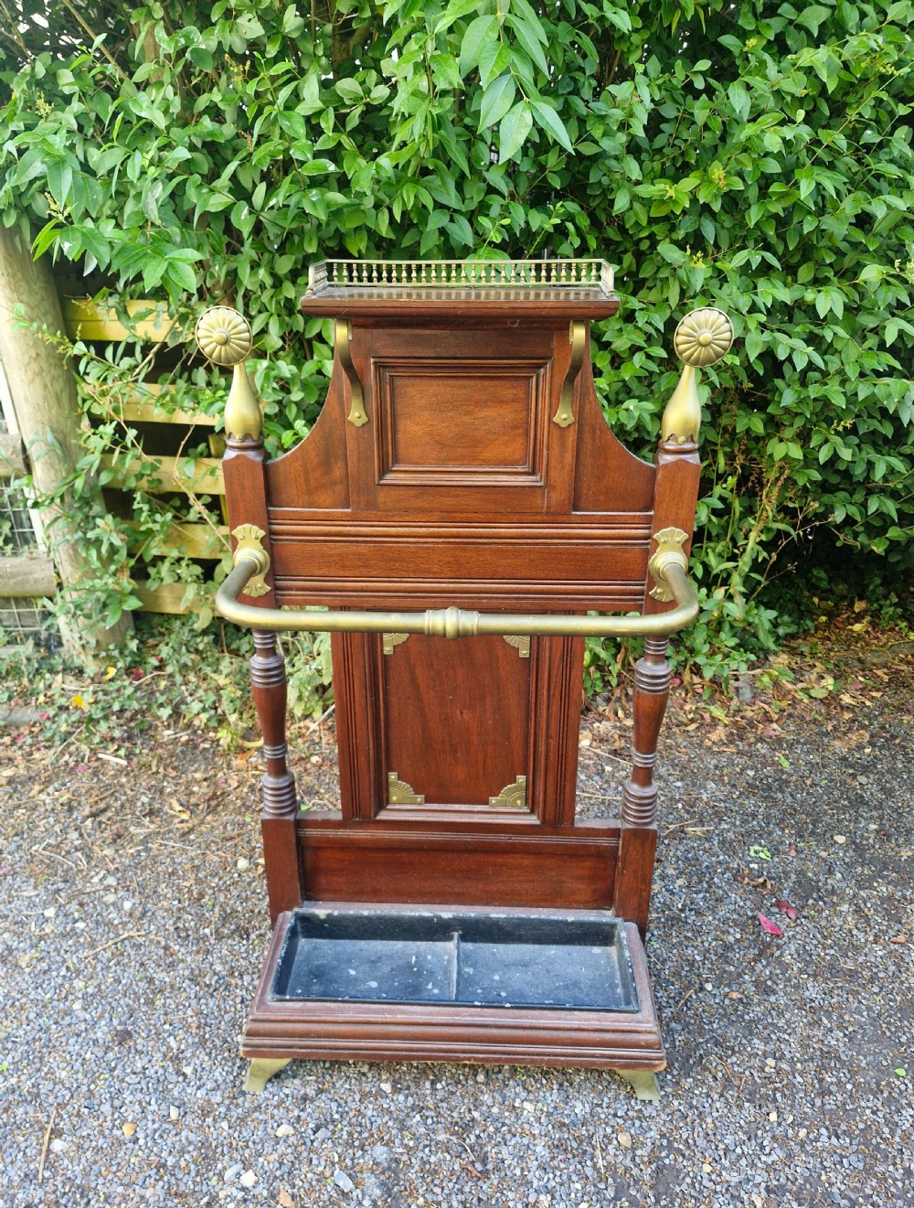 Late Victorian mahogany stick and umbrella stand featuring brass rails, decorative finials, a top gallery shelf, and a cast iron drip tray.