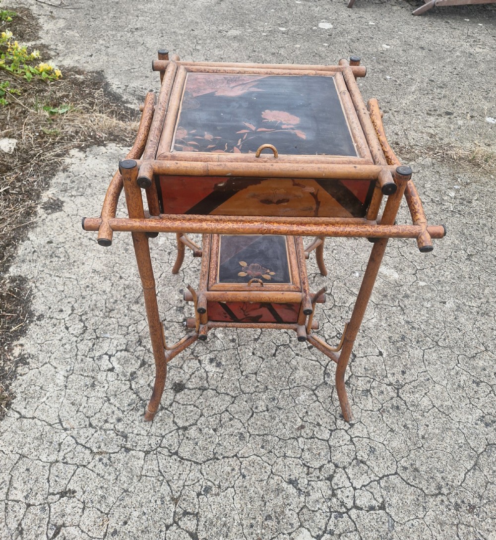 A two-tier Victorian tiger bamboo table with dark lacquered panels featuring floral decorations.