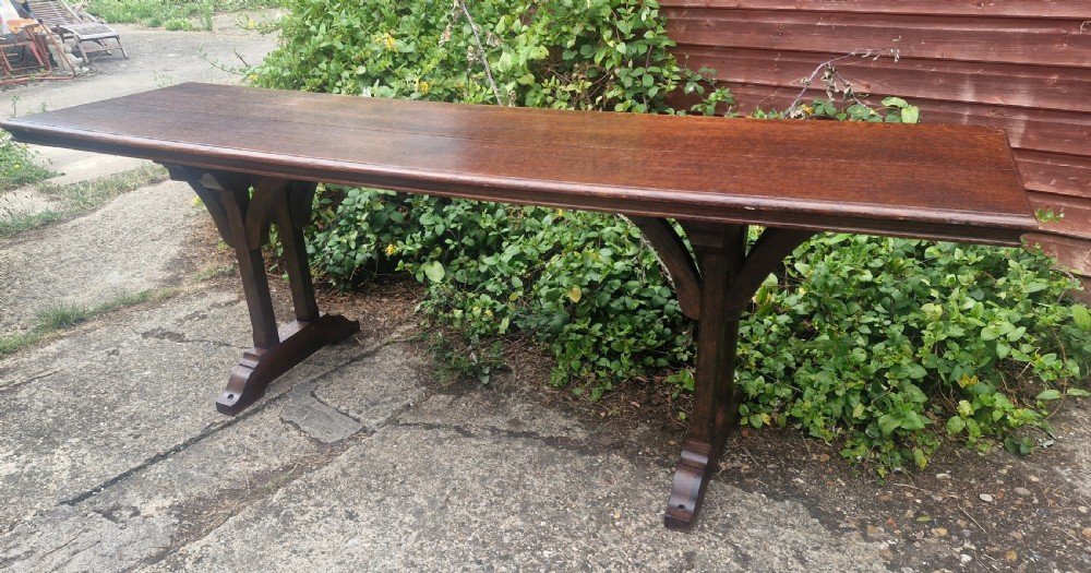 A long, narrow dark oak console table featuring a raised gallery edge and a Gothic architectural trestle underframe.