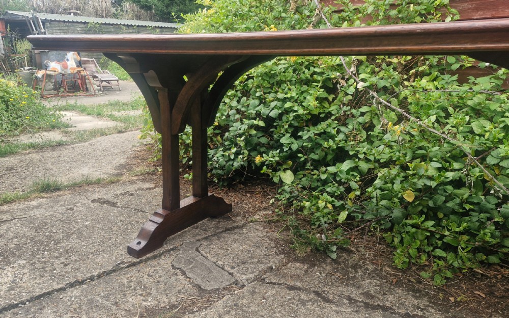 A long, narrow dark oak console table featuring a raised gallery edge and a Gothic architectural trestle underframe. View II