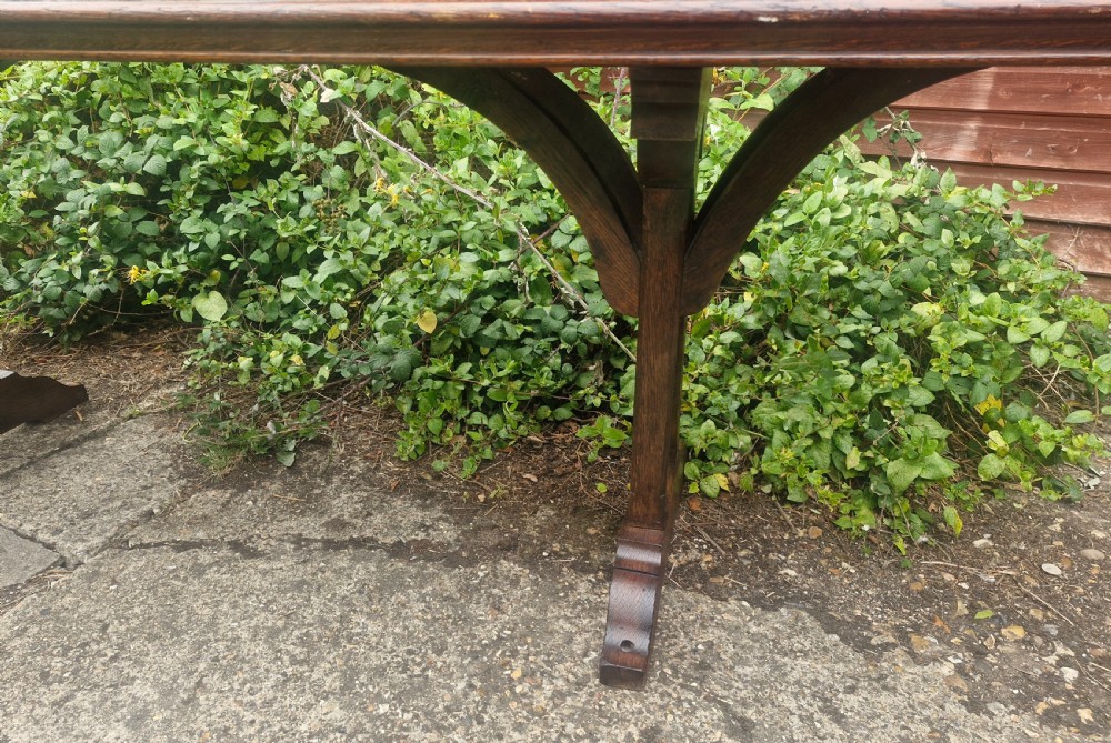 A long, narrow dark oak console table featuring a raised gallery edge and a Gothic architectural trestle underframe. View III