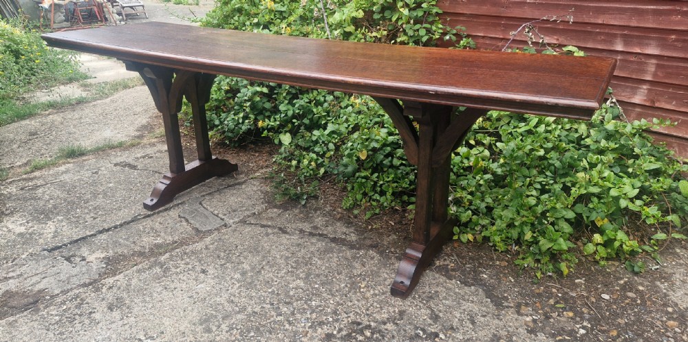 A long, narrow dark oak console table featuring a raised gallery edge and a Gothic architectural trestle underframe. View V