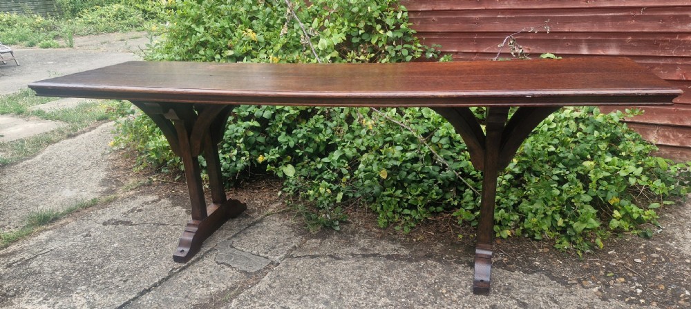 A long, narrow dark oak console table featuring a raised gallery edge and a Gothic architectural trestle underframe. View VI