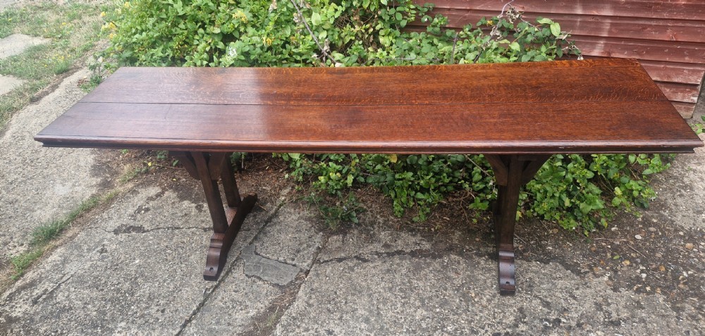 A long, narrow dark oak console table featuring a raised gallery edge and a Gothic architectural trestle underframe. View VII