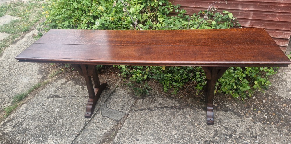 A long, narrow dark oak console table featuring a raised gallery edge and a Gothic architectural trestle underframe. View VIII