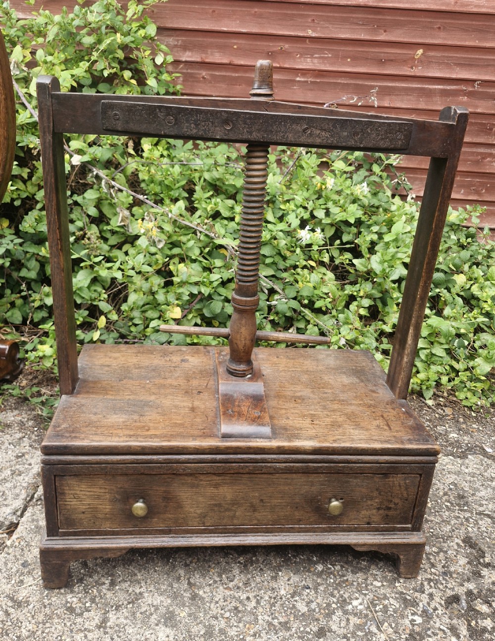 An antique Georgian dark oak tabletop book press featuring a central wooden threaded screw stem, an upper frame, and a base drawer with brass knobs.