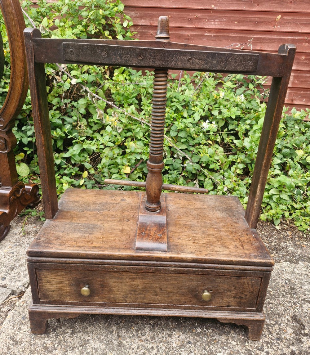 An antique Georgian dark oak tabletop book press featuring a central wooden threaded screw stem, an upper frame, and a base drawer with brass knobs. View IX