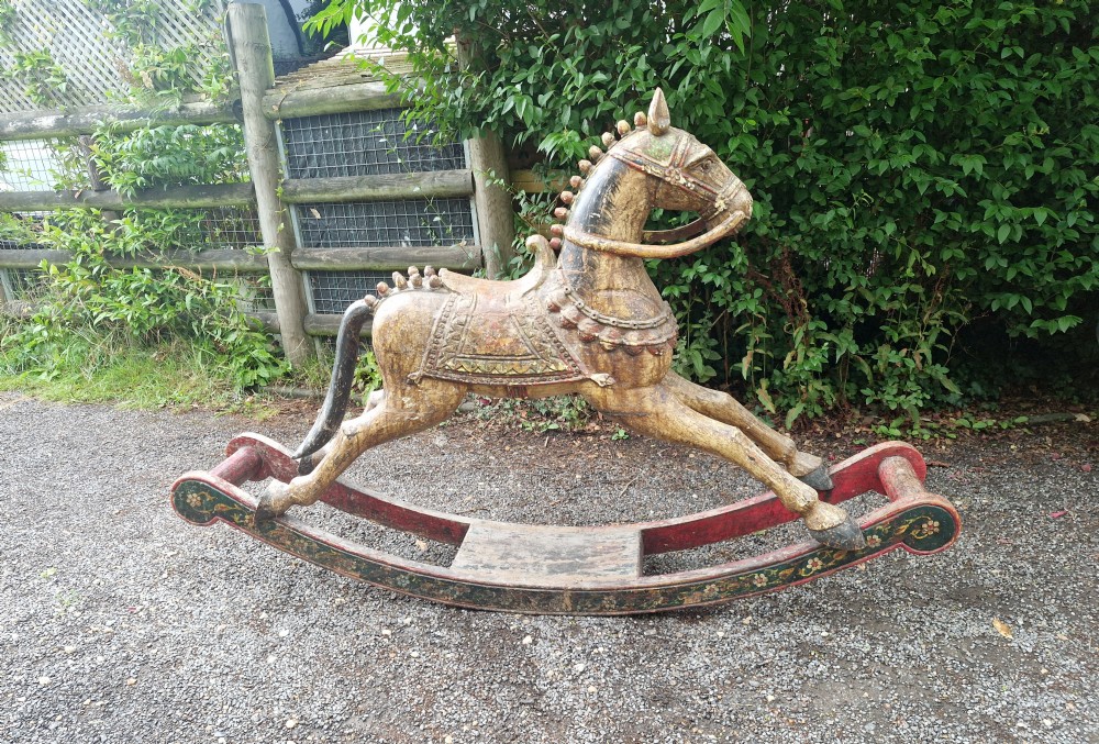 A hand-carved wooden rocking horse with polychrome painted decoration, carved harness detailing, and curved red wooden bow rockers.