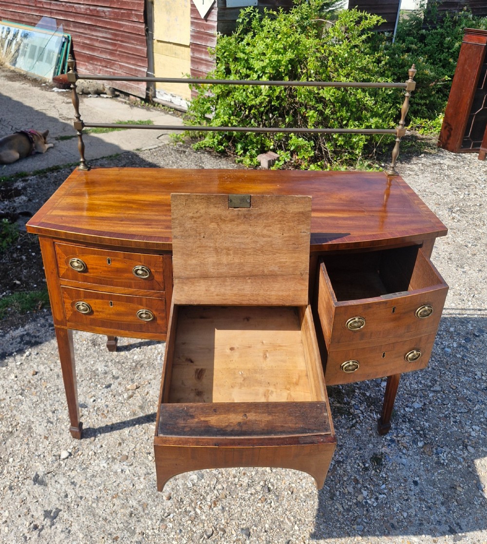 A late Georgian bowfront mahogany sideboard featuring boxwood inlay, brass ring handles, tapered legs, and a fitted brass gallery rail. View II