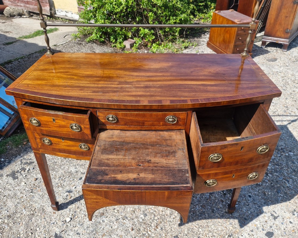 A late Georgian bowfront mahogany sideboard featuring boxwood inlay, brass ring handles, tapered legs, and a fitted brass gallery rail. View V
