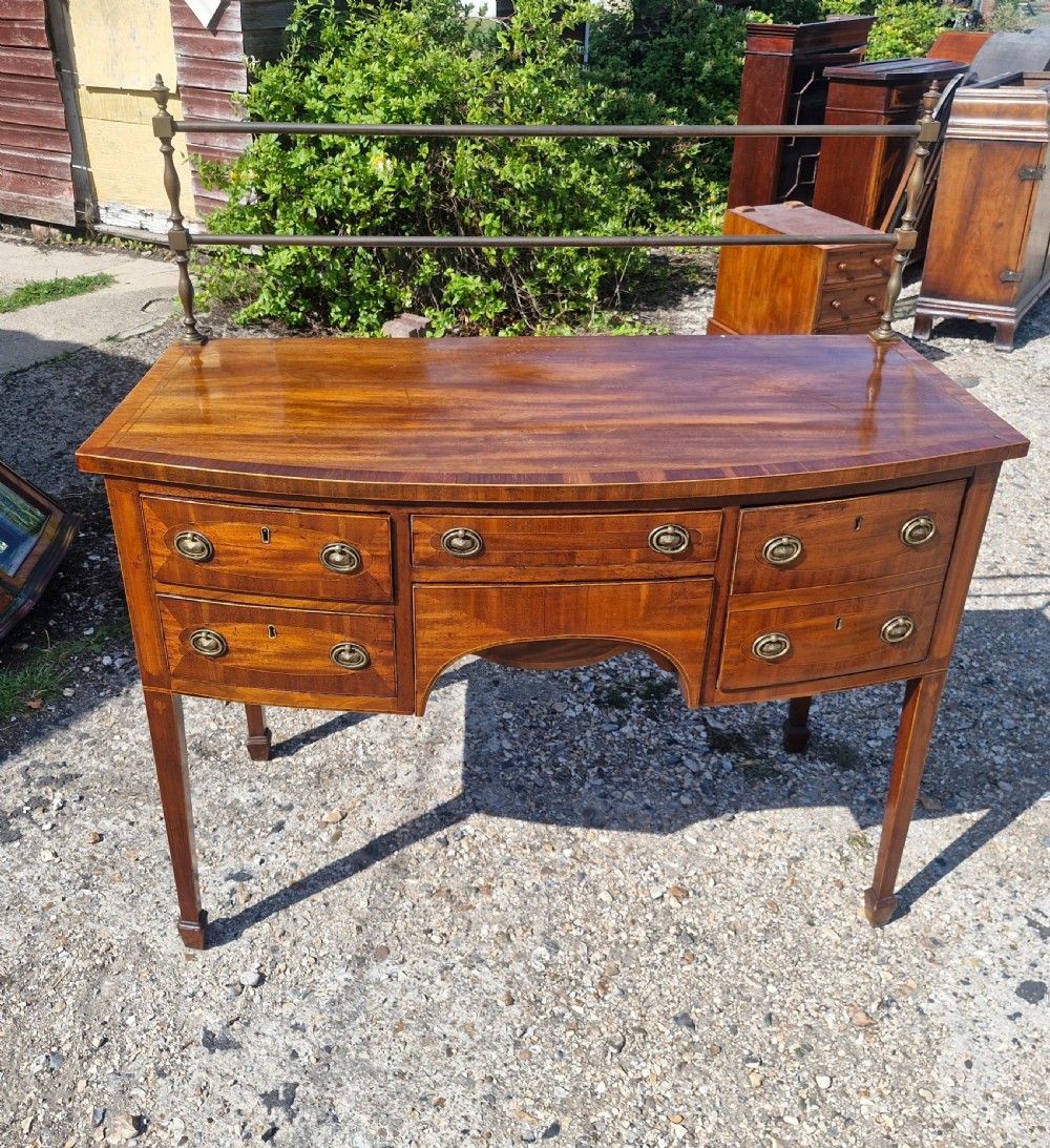 A late Georgian bowfront mahogany sideboard featuring boxwood inlay, brass ring handles, tapered legs, and a fitted brass gallery rail. View VI
