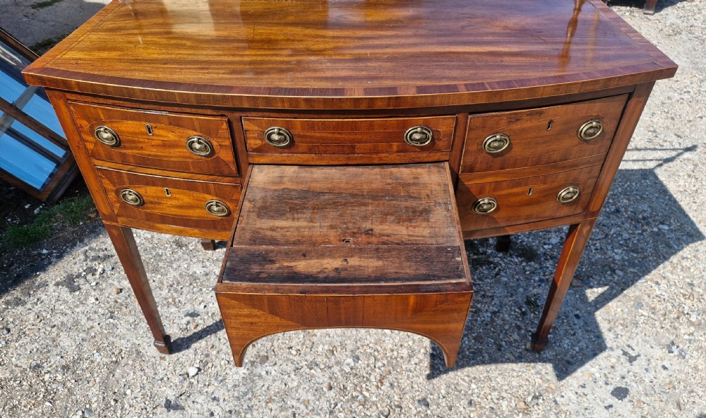 A late Georgian bowfront mahogany sideboard featuring boxwood inlay, brass ring handles, tapered legs, and a fitted brass gallery rail. View VII