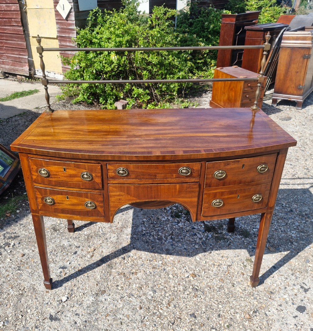 A late Georgian bowfront mahogany sideboard featuring boxwood inlay, brass ring handles, tapered legs, and a fitted brass gallery rail. View VIII