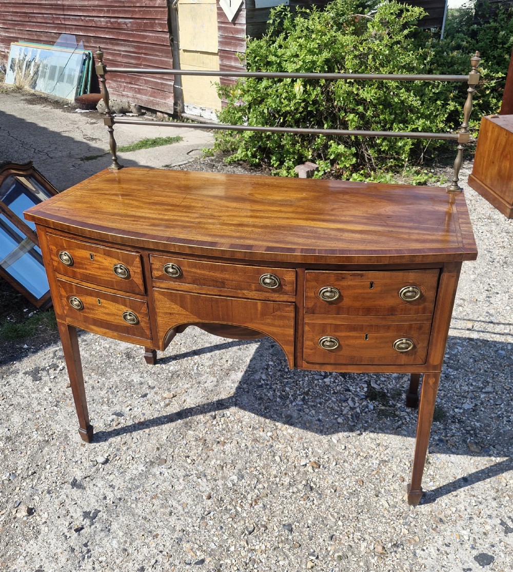 A late Georgian bowfront mahogany sideboard featuring boxwood inlay, brass ring handles, tapered legs, and a fitted brass gallery rail. View IX