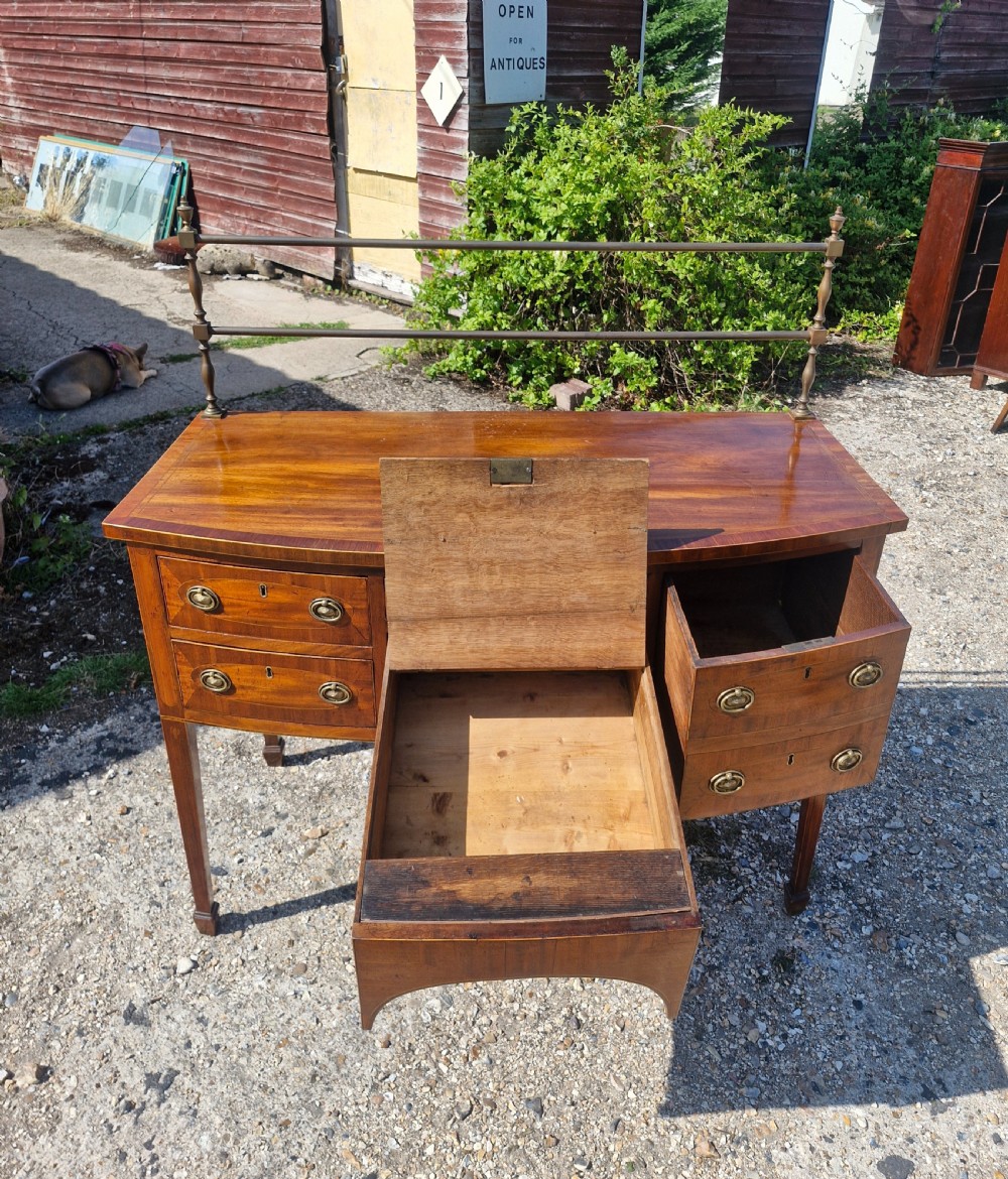 A late Georgian bowfront mahogany sideboard featuring boxwood inlay, brass ring handles, tapered legs, and a fitted brass gallery rail. View X