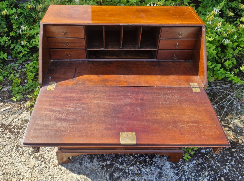 A late Georgian mahogany writing bureau featuring a sloped fall-front lid with boxwood inlay, four long drawers, brass swan-neck handles, and bracket feet. View VII