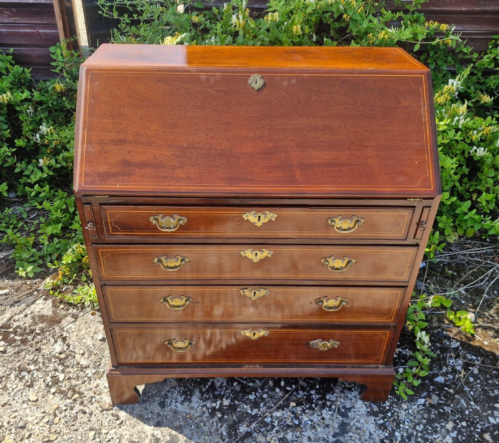 A late Georgian mahogany writing bureau featuring a sloped fall-front lid with boxwood inlay, four long drawers, brass swan-neck handles, and bracket feet. View VIII