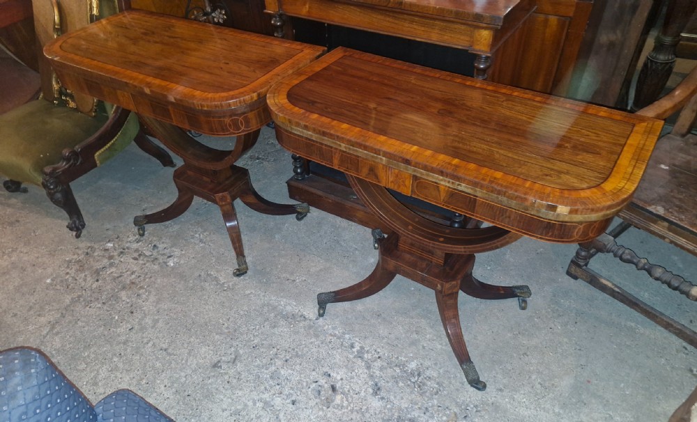 A matching pair of Regency rosewood tea tables featuring inlaid crossbanded fold-over tops supported by curved pedestals on four splayed legs with brass castors. View V