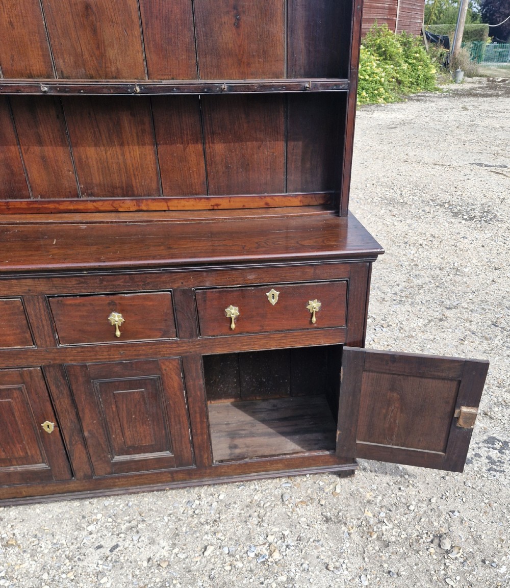 A nineteenth-century dark oak Welsh dresser featuring a scalloped upper plate rack above three drawers and three panelled cupboard doors with brass handles. View II