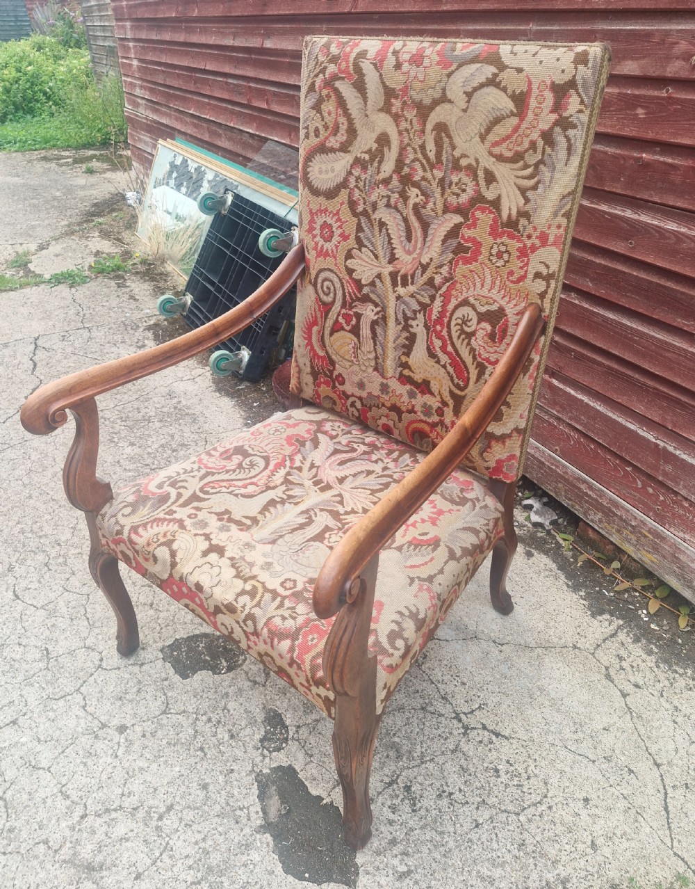 A high-backed open armchair upholstered in patterned tapestry depicting mythical bird motifs, supported by carved wooden cabriole legs.