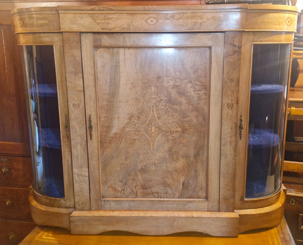 A Victorian walnut side cabinet featuring a central inlaid timber door flanked by two curved glazed display sections with velvet interior shelves.