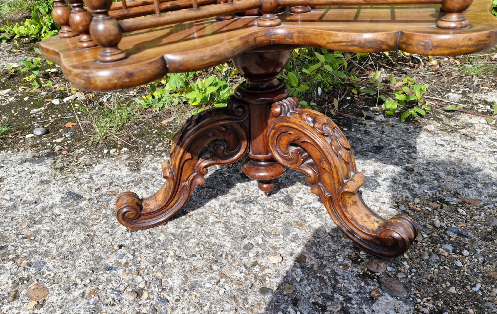 A nineteenth century revolving wooden booktable featuring tiered shelves with spindle galleries, a central turned column, and an ornate carved base. View VI