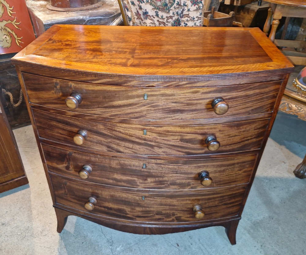 An early 19th-century mahogany bow front chest of drawers featuring four graduated drawers with turned wooden knobs and splayed feet.
