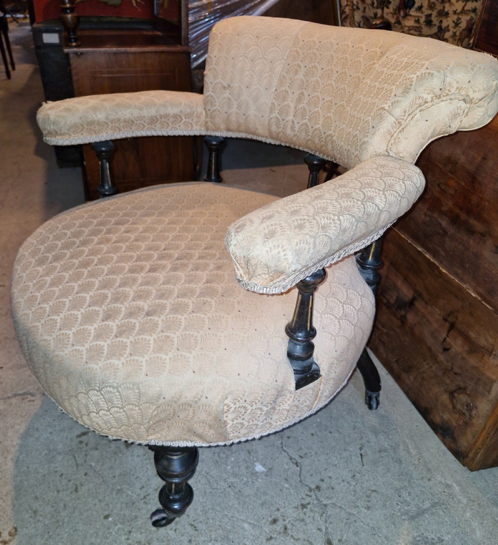 A late Victorian tub chair with cream patterned upholstery, turned ebonised wood arm supports, turned legs, and metal castors.