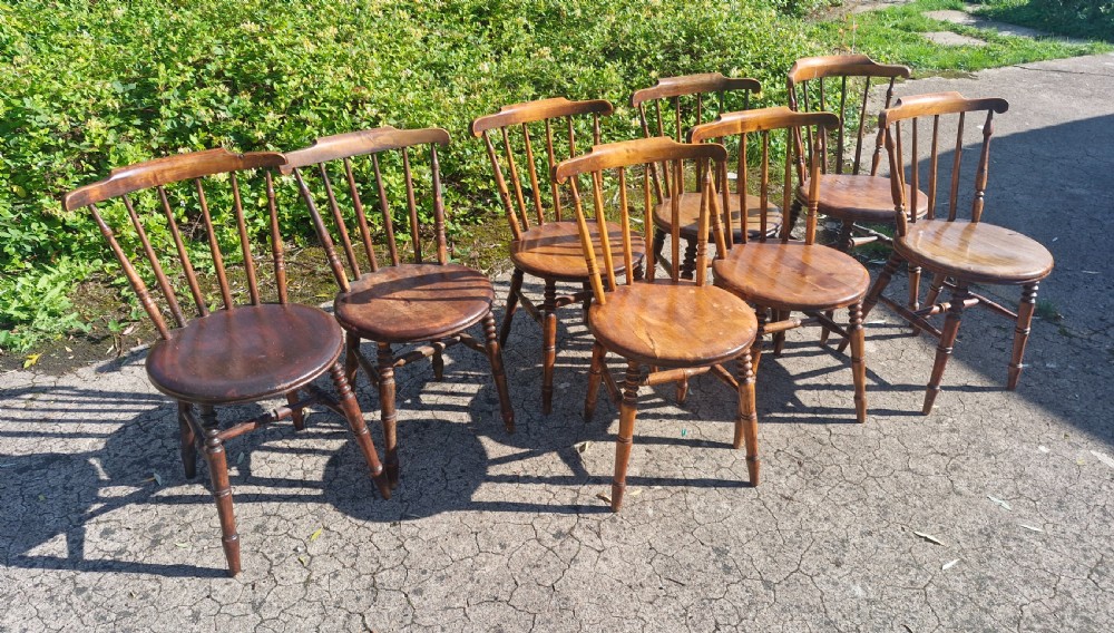 A set of eight matched antique wooden kitchen chairs featuring circular seats, spindle backs, curved crest rails, and turned legs. View V