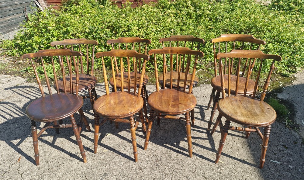 A set of eight matched antique wooden kitchen chairs featuring circular seats, spindle backs, curved crest rails, and turned legs. View VII