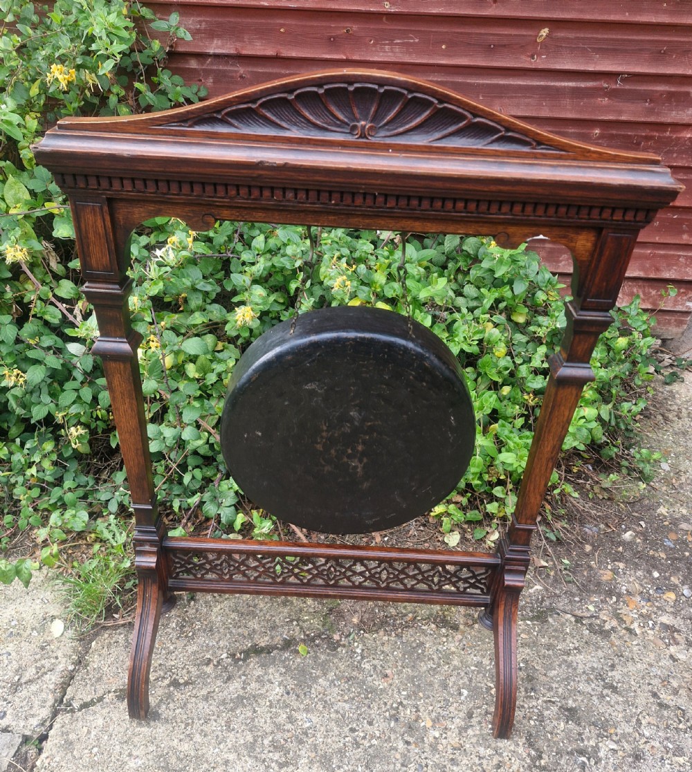 A Victorian carved oak floor-standing frame featuring a shell-carved pediment and open fretwork base, holding a suspended circular metal gong.