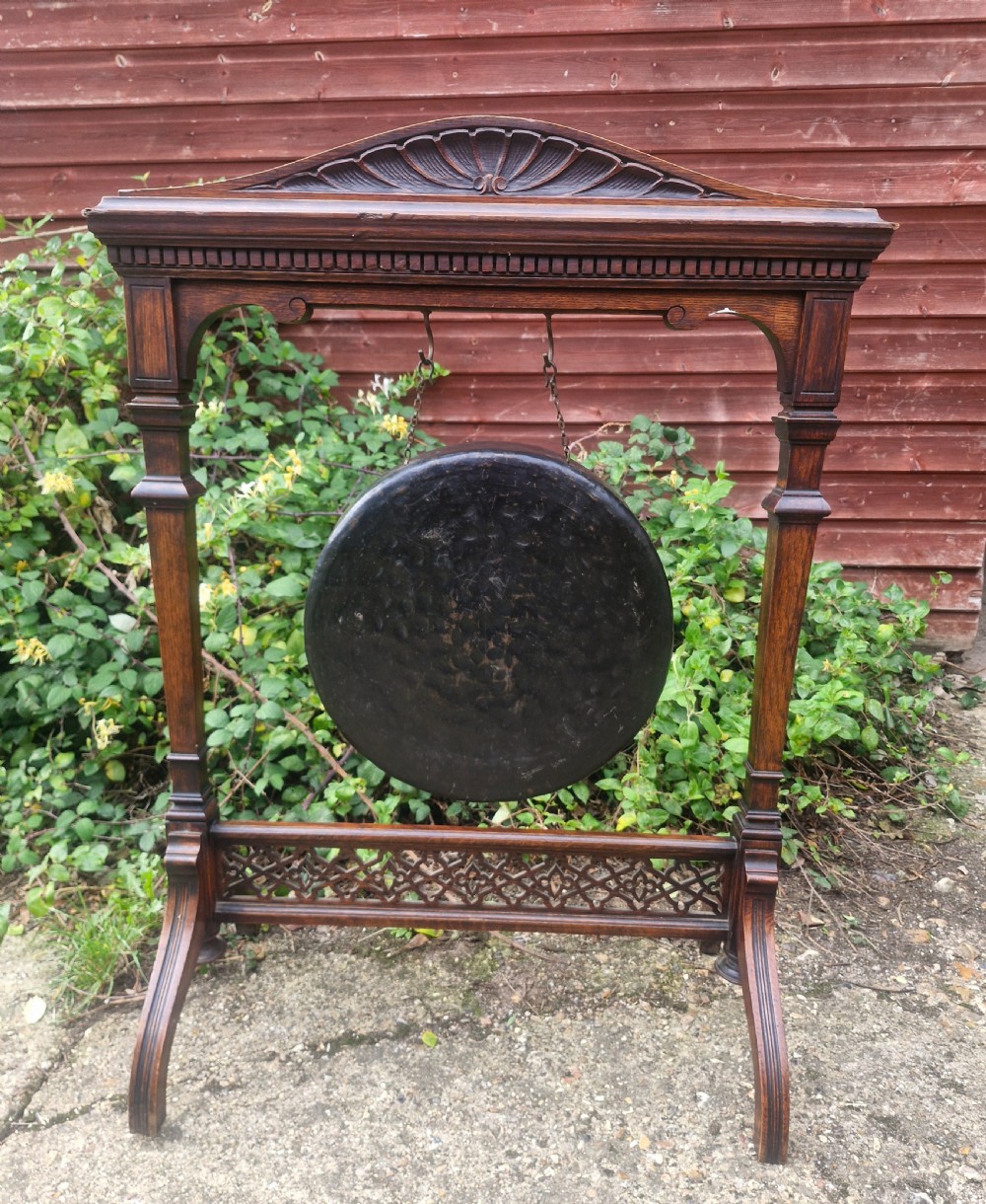 A Victorian carved oak floor-standing frame featuring a shell-carved pediment and open fretwork base, holding a suspended circular metal gong. View II