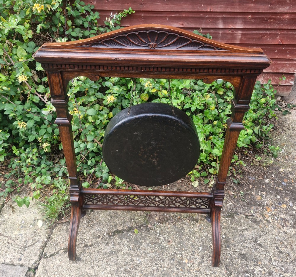 A Victorian carved oak floor-standing frame featuring a shell-carved pediment and open fretwork base, holding a suspended circular metal gong. View IV