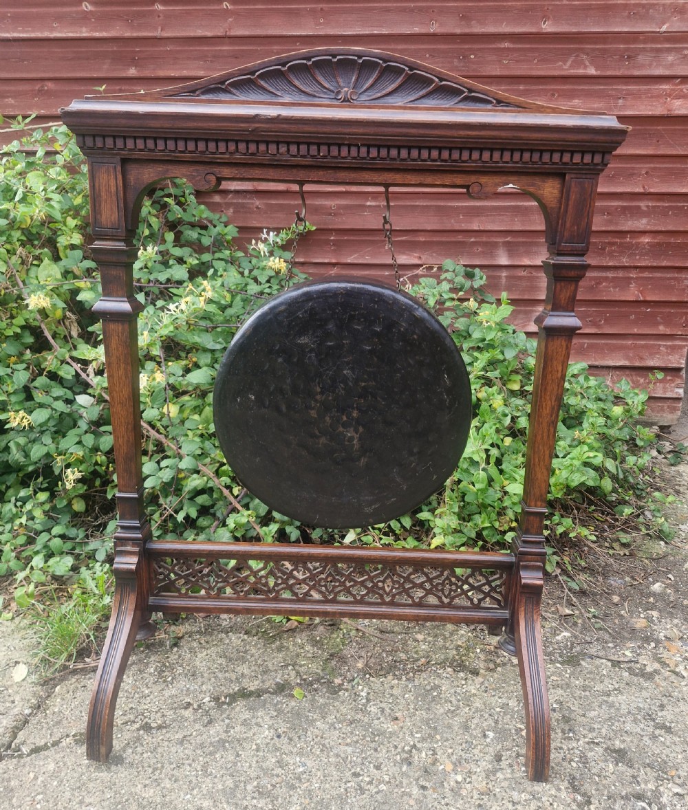 A Victorian carved oak floor-standing frame featuring a shell-carved pediment and open fretwork base, holding a suspended circular metal gong. View V
