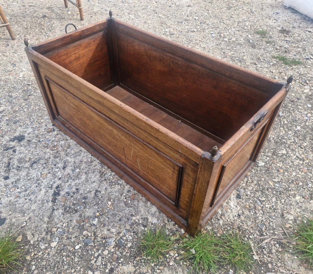 A rectangular wooden log bin with panelled sides, brass corner finials, and metal carrying handles. View II