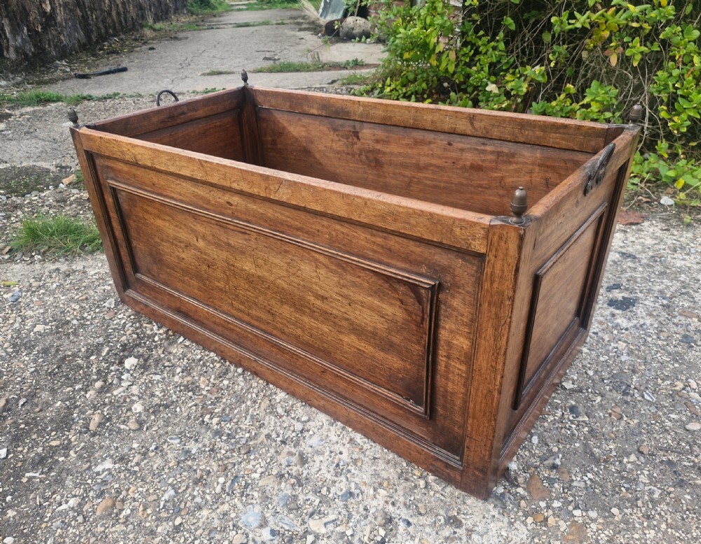 A rectangular wooden log bin with panelled sides, brass corner finials, and metal carrying handles. View III