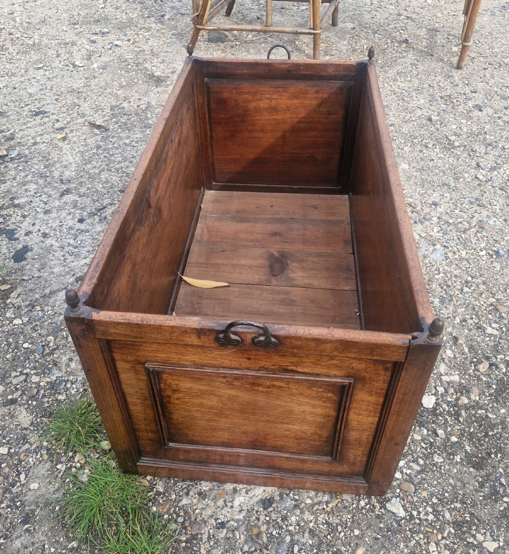 A rectangular wooden log bin with panelled sides, brass corner finials, and metal carrying handles. View IV