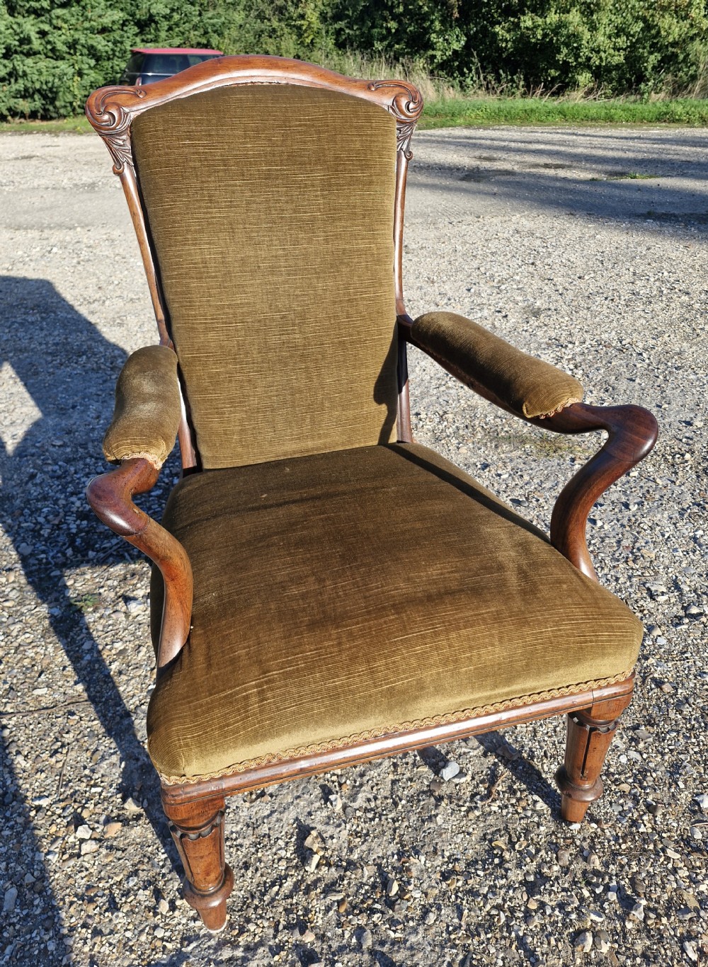 An Early Victorian rosewood armchair featuring olive green velvet upholstery, carved cresting rail, padded armrests, and turned front legs.
