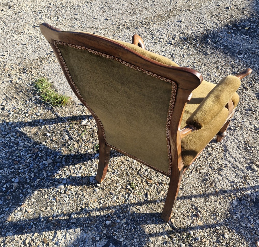 An Early Victorian rosewood armchair featuring olive green velvet upholstery, carved cresting rail, padded armrests, and turned front legs. View III